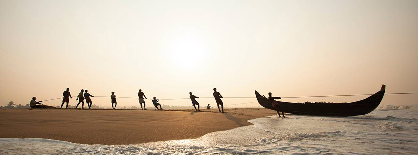 Ten fisherman use ropes to pull a small boat out of the water and onto a beach.